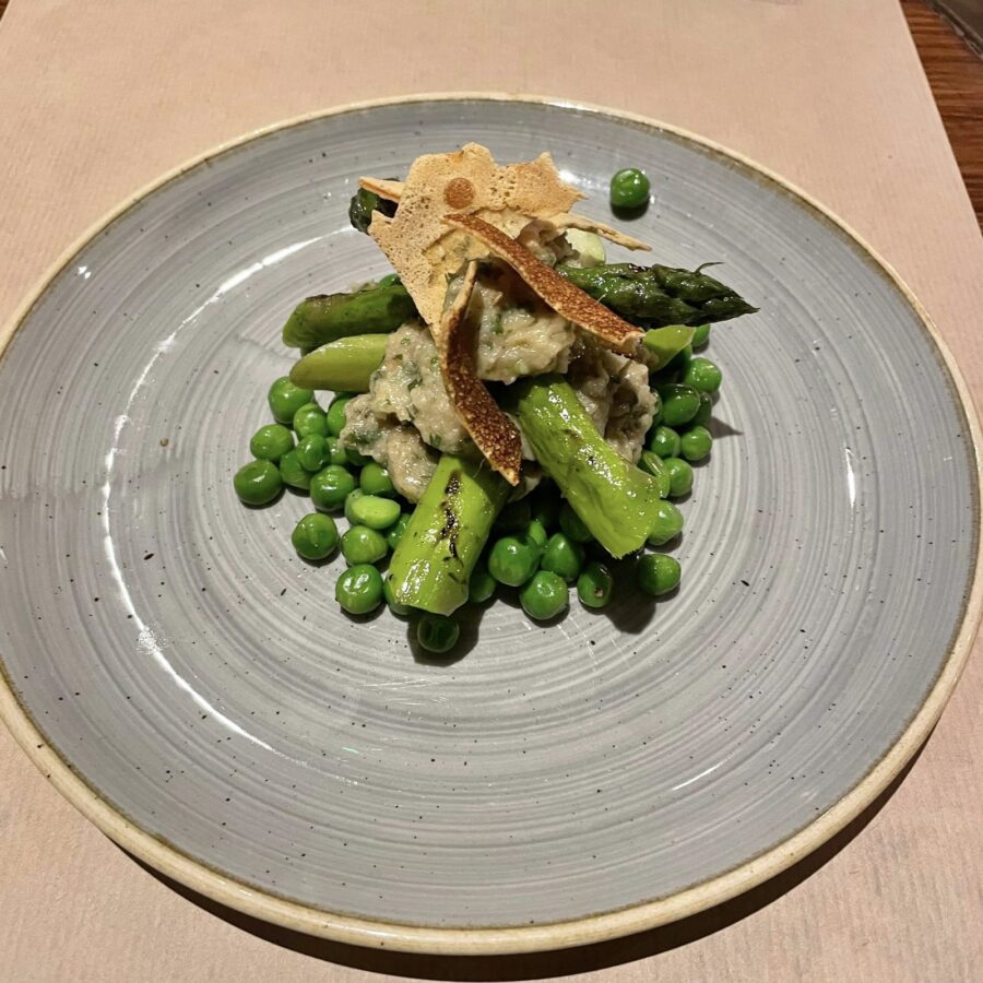 Asparagus with smoky chickpea and mint crisps and fresh spring vegetables accompanied by a bright yellow egg