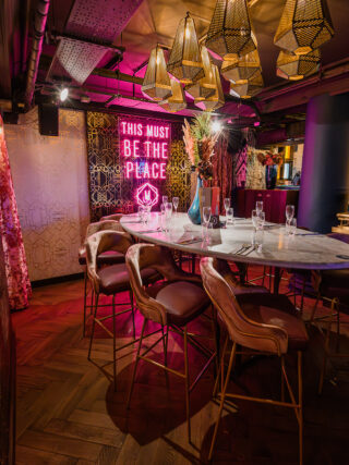 Round table and high chairs set with wine glasses and cutlery under drop lighting