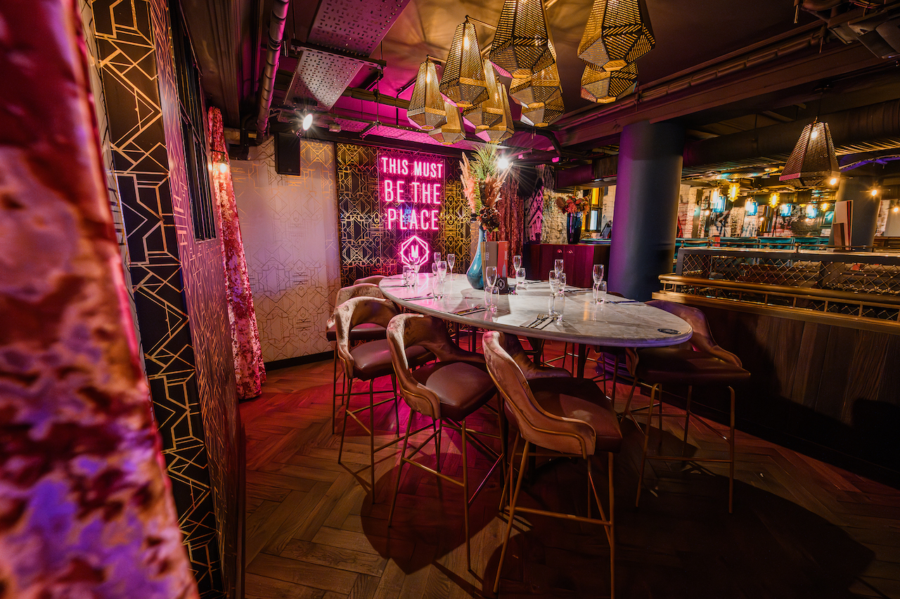 Round table and high chairs set with wine glasses and cutlery under drop lighting