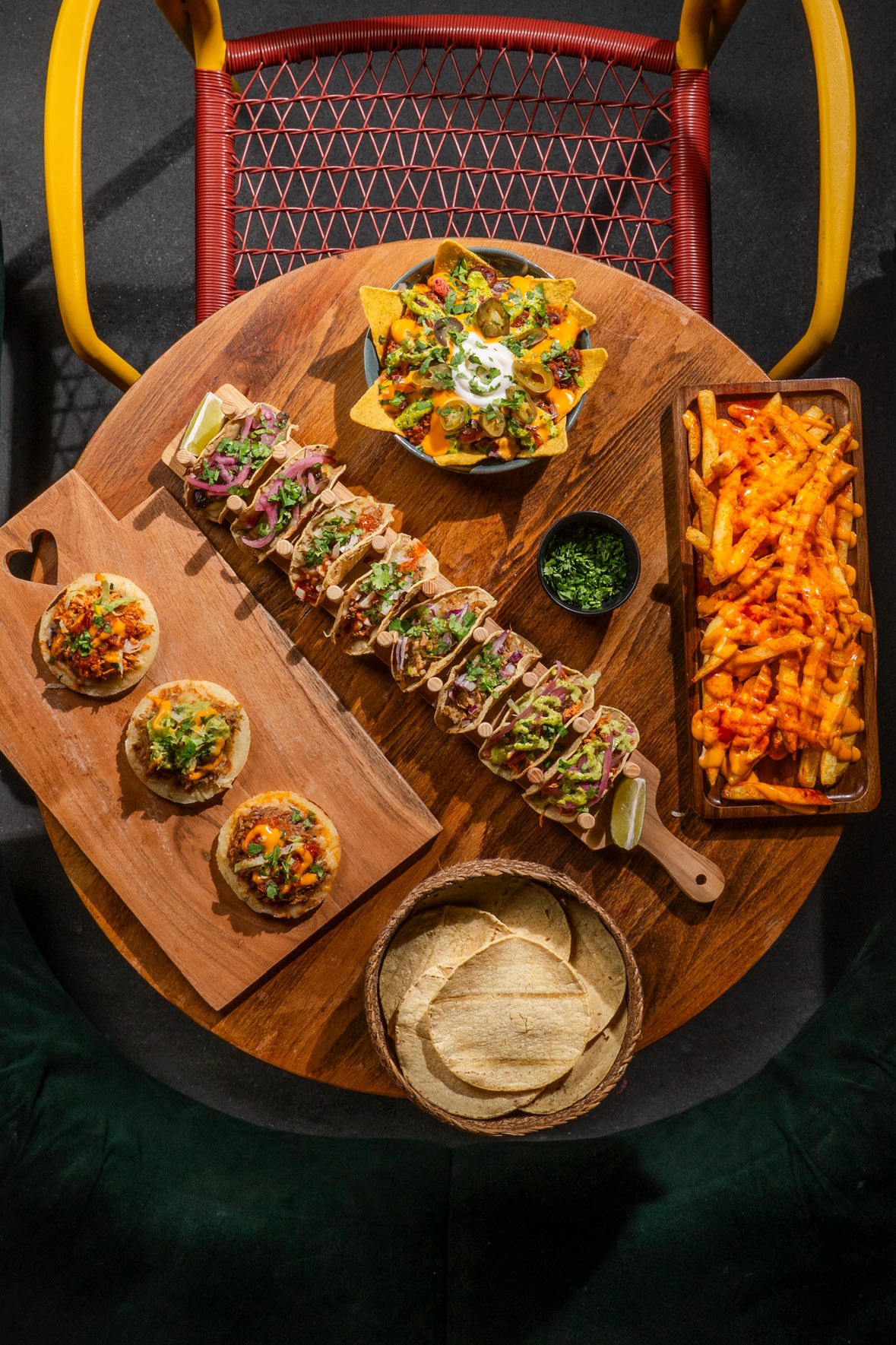 A table laid out with nachos, several tacos on a tray, dips and fries at Motel Mexicana