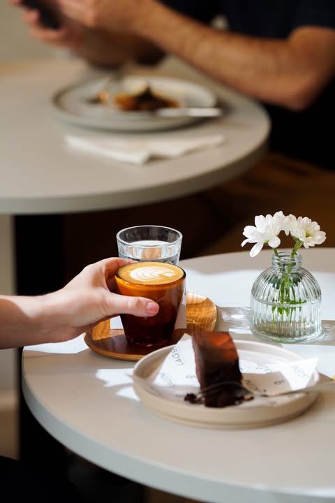 The hand of someone picking up a coffee cup next to a cake at Lagom