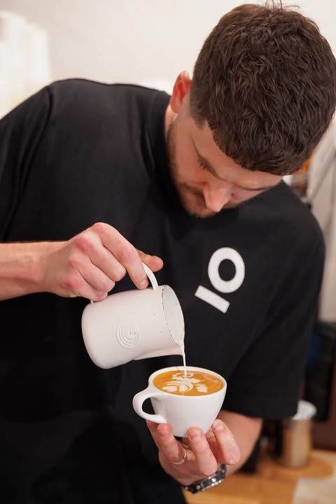 The barista at Lagom pouring the milk and creating art on the top of the coffee